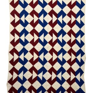 May include: A handmade quilt with a repeating geometric pattern. The design features alternating blocks of white, deep red, and blue. The quilt is made of fabric and has a stitched texture, perfect for a bed or sofa.