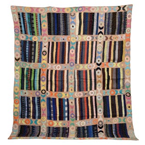 May include: A rectangular textile quilt featuring a grid of dark, multi-colored striped fabric panels separated by light tan bands. The tan bands are decorated with repeating circular and geometric embroidery in various bright colors.