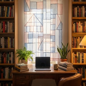 May include: A home office with a wooden desk, a laptop, and a leather chair. The desk is positioned in front of a window with a geometric patterned curtain. Bookshelves flank the window, filled with books. Potted plants add a touch of greenery.