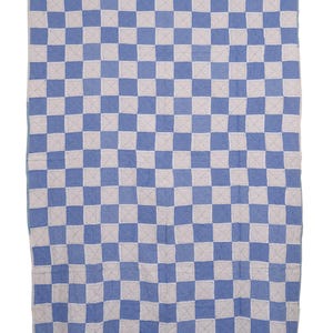 May include: A rectangular quilt featuring a repeating checkerboard pattern of light blue and off-white squares. The fabric surface displays visible, fine white stitching that forms an 'X' shape within each individual square across the entire textile.