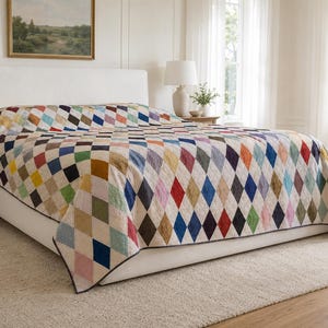 Könnte beinhalten: Eine Tagesdecke mit einem sich wiederholenden Rautenmuster in verschiedenen Farben wie Rot, Blau, Grün, Gelb und Rosa auf cremefarbenem Hintergrund. Der Quilt bedeckt ein großes Bett und zeigt ein geometrisches Design auf der gesamten Fläche.