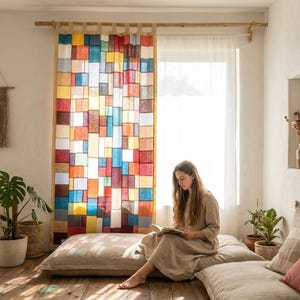 Puede incluir: Una colorida cortina de patchwork, compuesta por rectángulos de tela multicolores, cuelga frente a una ventana. Una mujer está sentada en un cojín en el suelo, leyendo un libro. La habitación tiene una estética natural y bohemia. La cortina presenta tonos rojos, azules, amarillos y naranjas.