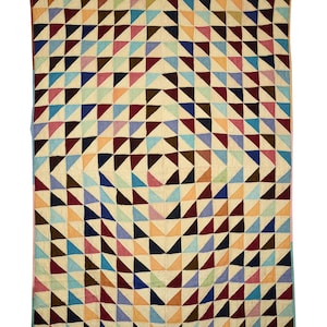 May include: A handmade quilt with a geometric pattern of colorful triangles. The quilt features a cream-colored background with triangles in shades of blue, red, brown, pink, and orange. The quilt is rectangular and appears to be made of fabric.