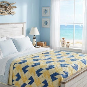 Puede incluir: Un dormitorio con temática costera. La cama tiene un edredón con estampado geométrico amarillo y azul, almohadas blancas y un cabecero blanco. Una lámpara de faro está en la mesita de noche. La ventana da al mar.