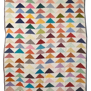 May include: A colorful quilt featuring a repeating pattern of triangles in various colors, including red, blue, yellow, and green. The triangles are arranged on a cream-colored background, with a dark brown border. This handmade quilt is a cozy home decor item.