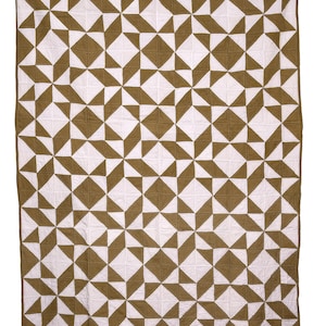 May include: A large, geometric quilt featuring a repeating pattern of olive green and white shapes. The quilt is rectangular and appears to be made of stitched fabric, suitable for a bed or wall hanging.