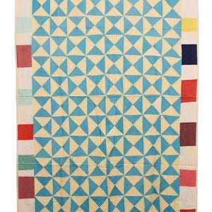 May include: A handmade quilt with a geometric pattern of blue triangles on a cream background. The border features a patchwork design with squares of various colours. The text "VL1898" is at the bottom.