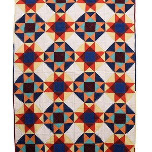 Könnte beinhalten: Ein farbenfroher Quilt mit einem geometrischen Sternmuster. Der Quilt hat einen weißen Hintergrund mit sich wiederholenden Quadraten aus roten, orangefarbenen, blauen und türkisfarbenen Sternenmustern. Die Kanten sind mit einem dunkelroten Rand versehen.