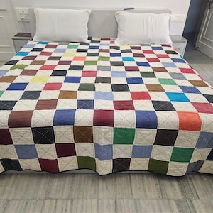 Puede incluir: Una cama cubierta con un edredón de retazos con un patrón de tablero de ajedrez de varios colores, incluyendo rojo, azul, verde y marrón. Dos almohadas blancas descansan sobre la cama. El edredón está hecho de cuadrados cosidos con hilo blanco.