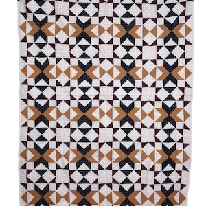 Könnte beinhalten: Eine geometrische Steppdecke mit einem sich wiederholenden Muster aus sternartigen Formen in Weiß, Schwarz, Braun und Burgunderrot. Die Steppdecke hängt vor einem weißen Hintergrund und zeigt die detaillierten Nähte und die Farbanordnung. Dieser Textilartikel eignet sich für die Heimdekoration.
