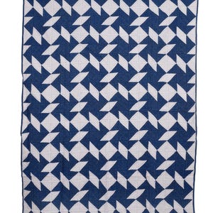 Puede incluir: Una manta rectangular con un patrón geométrico. El diseño presenta formas de diamante blancas y azul marino dispuestas en un patrón repetitivo. La manta tiene un borde azul marino.