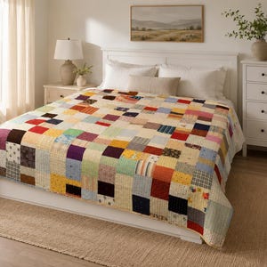 Puede incluir: Una colcha de retazos que presenta una cuadrícula de cuadrados de tela multicolores con varios patrones, incluyendo sólidos, rayas y flores. La colcha está extendida sobre una estructura de cama blanca, mostrando una diversa gama de colores como rojo, amarillo, azul y morado.