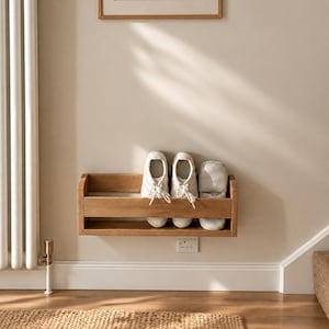 May include: A light-coloured wooden wall-mounted shelf with a horizontal rail, featuring a pair of black leather ankle boots with gold-tone side zips placed inside the shelf structure against a plain white wall background.