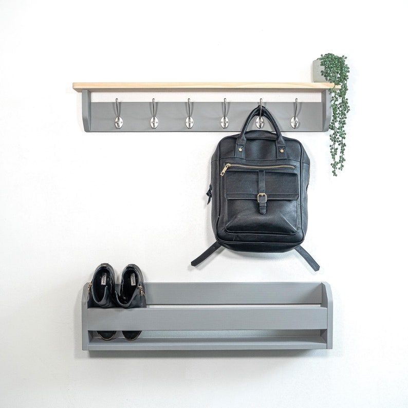 May include: Gray wooden shelf with hooks and a gray shoe shelf below. A black leather backpack hangs from the hooks. Two pairs of black shoes are on the shoe shelf.
