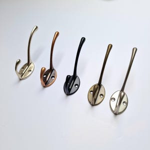 May include: Five metal hooks in different finishes: silver, copper, black, brass, and nickel. The hooks are all the same shape and size, with a curved hook and a round base.