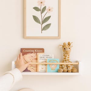 Floating white nursery shelf with oak pegs, stylish baby room organizer for clothes, toys and books