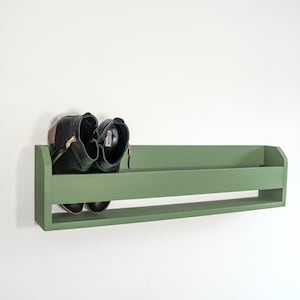 May include: A green wooden shelf with a pair of black boots on it. The shelf is mounted on a white wall.