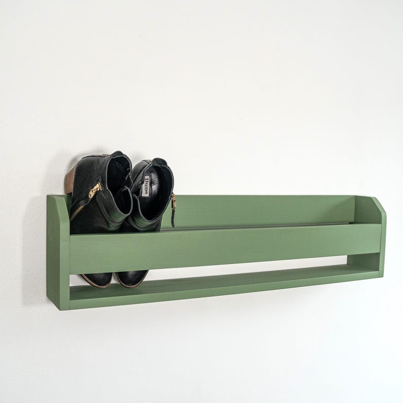 May include: A green wooden shelf with a pair of black boots on it. The shelf is mounted on a white wall.