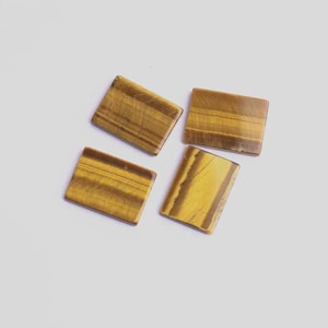 May include: Four rectangular tiger's eye gemstones. Each stone displays a mix of golden yellow and brown hues with natural striped patterns. The stones are arranged on a white surface.