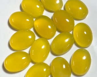 May include: A collection of twelve oval-shaped, polished gemstones in a vibrant yellow hue. The stones are smooth and reflective, with a glossy finish. The gemstones are arranged on a white surface, showcasing their color and shape.