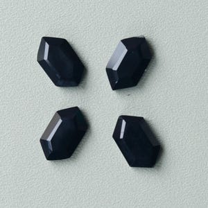 May include: Four black, faceted gemstones in a square arrangement. Each gem is rectangular with angled sides and a polished surface. The gems are displayed against a light grey background.