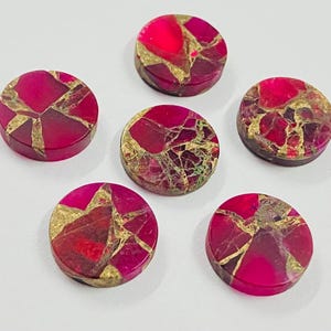 Puede incluir: Seis piedras preciosas redondas y pulidas con un patrón de mosaico en rojo, dorado y burdeos oscuro. Las piedras están dispuestas sobre una superficie blanca, mostrando sus colores vibrantes y texturas únicas. Adecuado para la fabricación de joyas.