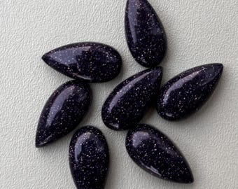 May include: Seven teardrop-shaped, polished gemstones. The stones are a deep blue with sparkling inclusions, resembling a starry night sky. The gems are arranged in a circular pattern, showcasing their smooth, glossy surfaces.