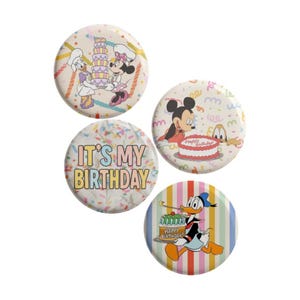 May include: Four circular pin-back buttons featuring Disney characters and birthday themes. One shows Daisy and Minnie with a cake, another Mickey and Pluto with a cake, one says IT'S MY BIRTHDAY with sprinkles, and one shows Donald with a cake.