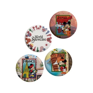 Op de afbeelding: Drie ronde buttons met Disney-thema's. Eén witte button toont de tekst World Showcase omringd door Mickey-vormige iconen met diverse nationale vlaggen. Twee andere buttons tonen Mickey Mouse met postzegels met de labels Japan, France en Italy.