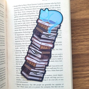 May include: A blue cat bookmark with a stack of books. The cat is sleeping on top of the stack of books. The bookmark is a great way to keep your place in your book.