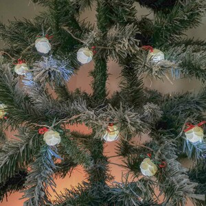 May include: A flocked artificial Christmas tree decorated with white string lights. The lights are shaped like small, round baubles and are strung throughout the branches of the tree.