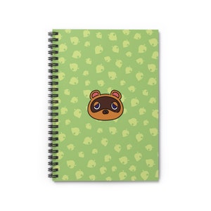 May include: A green spiral notebook with a repeating pattern of green leaves. A cartoon image of a brown raccoon with a sad expression is centred on the front cover.