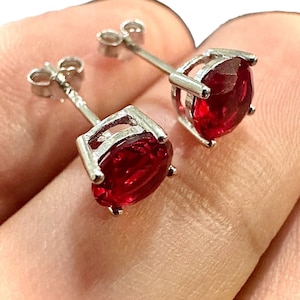 May include: A pair of silver stud earrings with red oval-shaped gemstones.