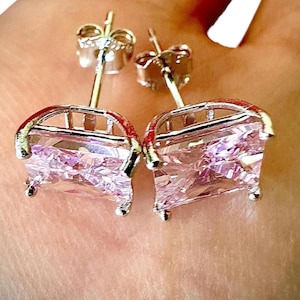 May include: A pair of silver-toned stud earrings. Each earring features a rectangular, faceted pink gemstone set within a decorative frame. The earrings have a post and butterfly backing for secure wear.