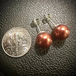 K&ouml;nnte beinhalten: Ein Paar Ohrstecker mit runden, dunkel kupferfarbenen Perlen und silberfarbenen Metallstiften, platziert neben einer amerikanischen Zehn-Cent-M&uuml;nze, um die Gr&ouml;&szlig;e der kugelf&ouml;rmigen Perlenelemente im Vergleich zu verdeutlichen.