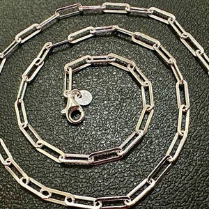May include: A silver chain necklace with a simple, linked design. The chain is made of small, rectangular links that are connected together to form a continuous loop.