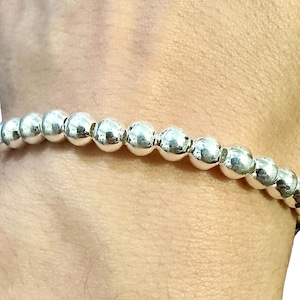 May include: A silver beaded bracelet with round beads. The bracelet is on a person's wrist.