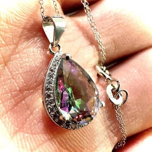 Pu&ograve; includere: Collana d'argento con un pendente a forma di goccia. Il pendente presenta una grande pietra iridescente, circondata da piccole pietre trasparenti. La delicata catena &egrave; d'argento.