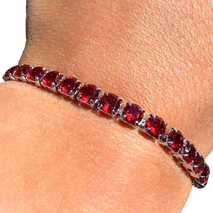 May include: A silver bracelet with square-cut, deep red gemstones. The bracelet is composed of a series of individual stones set closely together, creating a continuous line of color. The gemstones are a vibrant, saturated red.