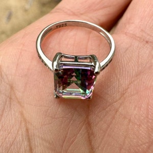 May include: A silver ring with a large, square-shaped, iridescent gemstone. The ring is marked with the number "Y925" on the band.
