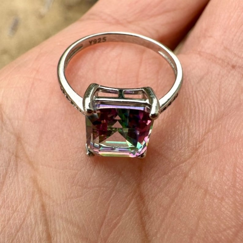 May include: A silver ring with a large, square-shaped, iridescent gemstone. The ring is marked with the number "Y925" on the band.