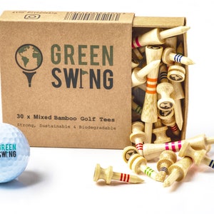 Op de afbeelding: Een doos met 30 gemengde bamboe golftees met kleurrijke strepen. De doos is bruin en heeft de tekst "GREEN SWING" erop gedrukt. De tees zijn sterk, duurzaam en biologisch afbreekbaar. Een golfbal met het "GREEN SWING" logo is ook te zien.