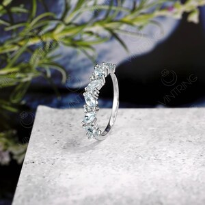 May include: A silver ring with a row of light blue marquise-shaped gemstones set in a delicate band.