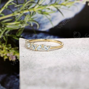 May include: A delicate gold band ring with a row of small, light blue gemstones. The ring is set on a white surface.
