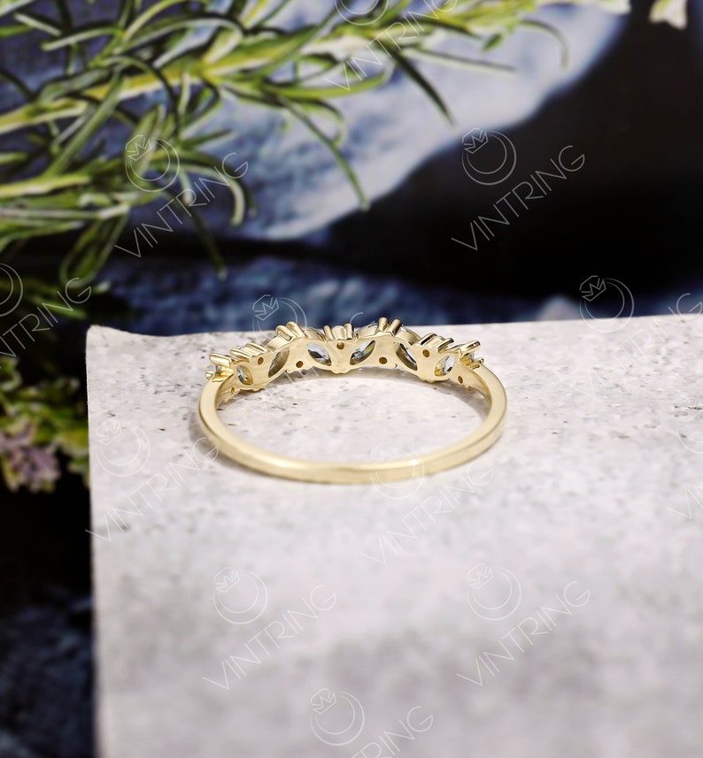May include: A gold band ring with a row of small, clear, marquise-shaped stones set in the band.