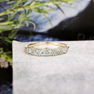 May include: A delicate gold band ring with a row of marquise-shaped aquamarine gemstones. The ring is set on a white background.