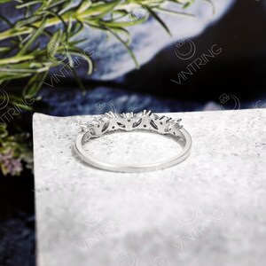 May include: A silver band ring with a row of small, clear gemstones set in a delicate, leaf-like design.