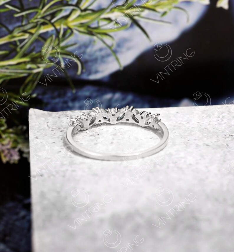 May include: A silver band ring with a row of small, clear gemstones set in a delicate, leaf-like design.