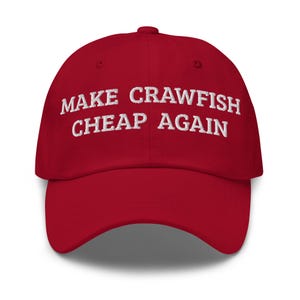 May include: A red baseball cap with the embroidered text "MAKE CRAWFISH CHEAP AGAIN" in white. The cap has a curved brim and a rounded crown. The hat is a solid, vibrant red color.