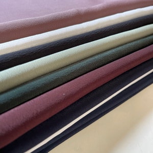 May include: A stack of fabric swatches in various colours, including dusty rose, white, black, sage green, dark green, burgundy, navy blue, and white.